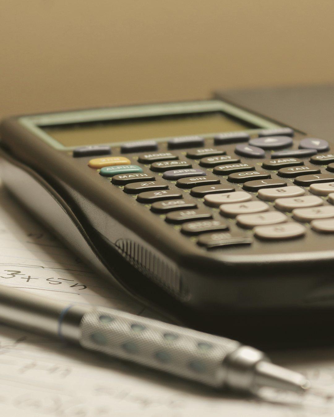 A calculator and a propelling pencil resting on a page of handwritten sums