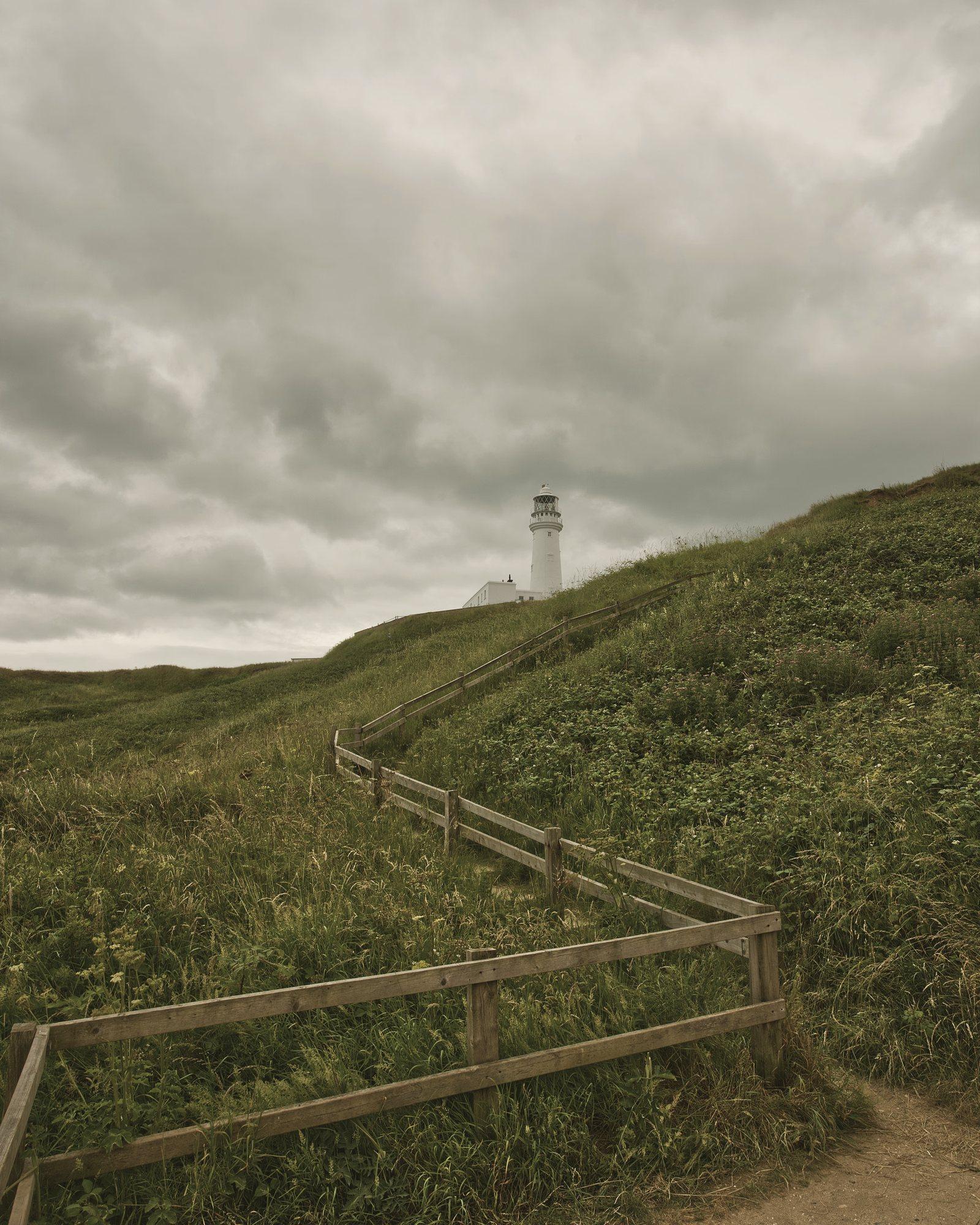 Flamborough Lighthouse atop a grassy slope, a fenced path leading up to it
