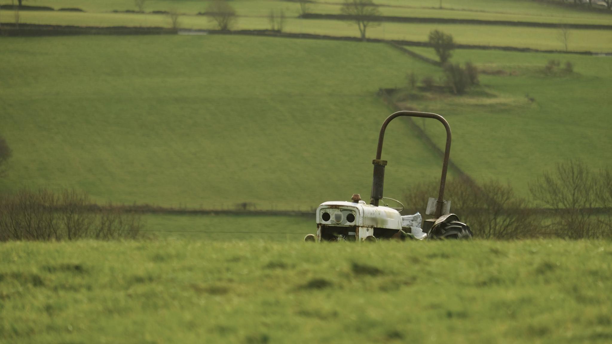 Old white tractor half hidden behind a grassy rise, stone-walled fields beyond