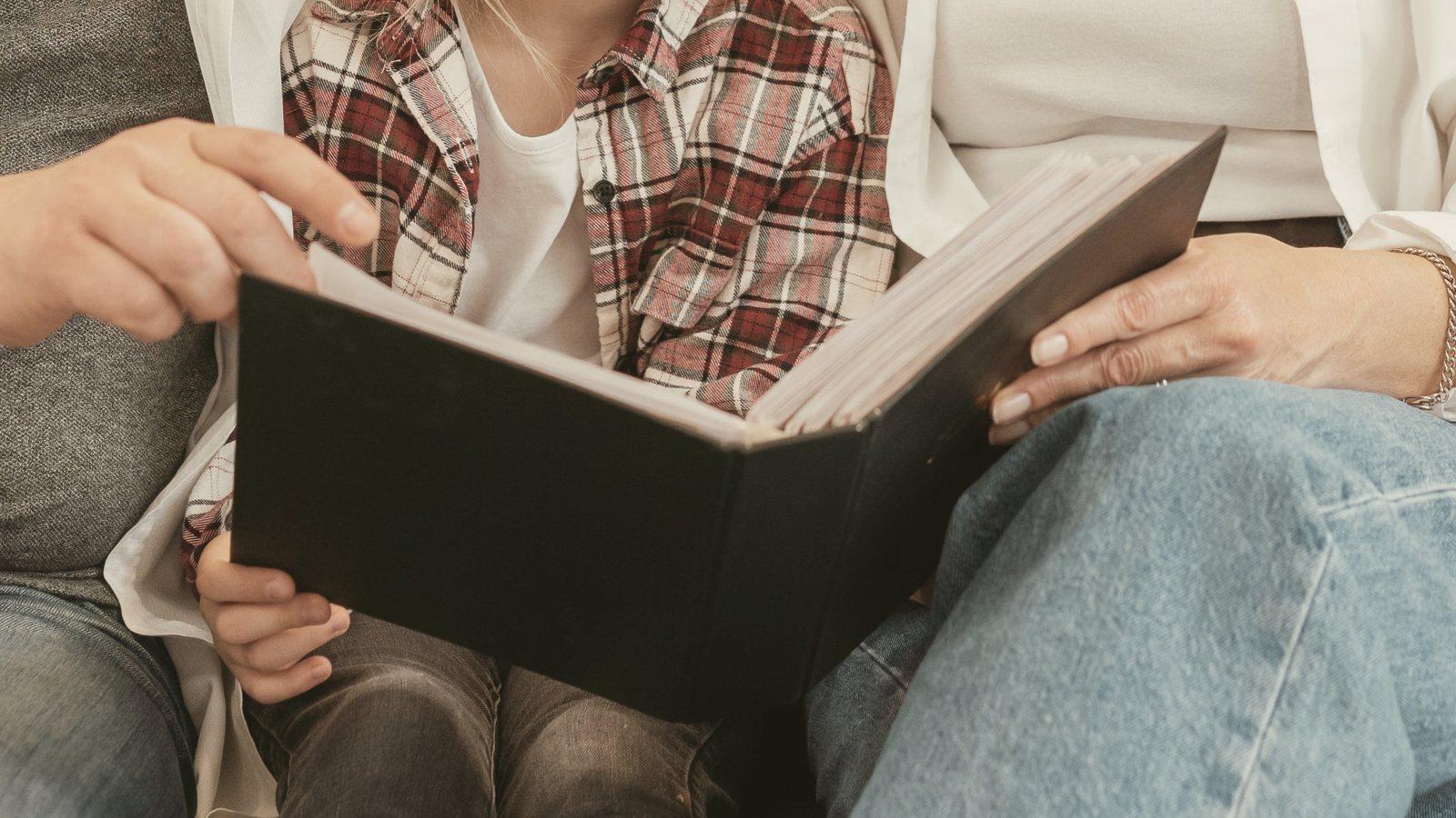 Grandparents' and a child's hands holding open a family photo album