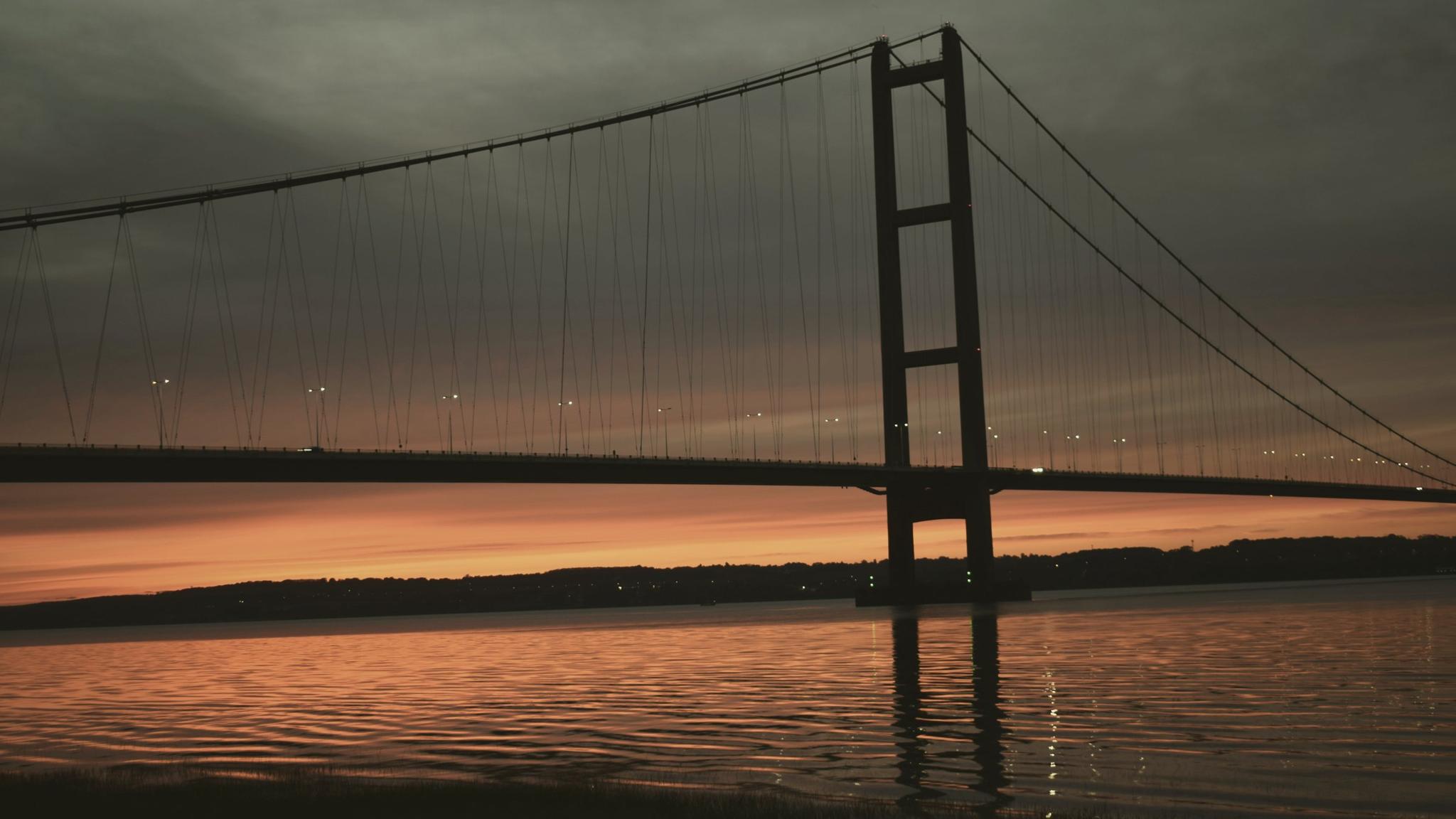 The Humber Bridge silhouetted against an orange dusk sky over the estuary