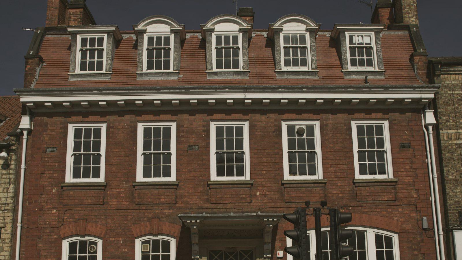 A three-storey red-brick building with dormer windows and two red telephone boxes on a market-town street