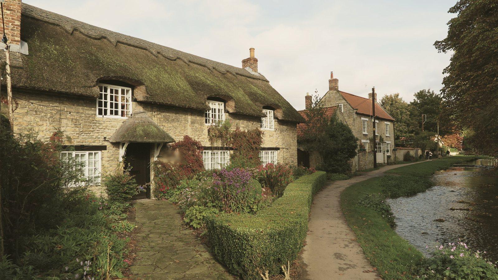 A thatched stone cottage with a flower garden beside a shallow beck and a footpath