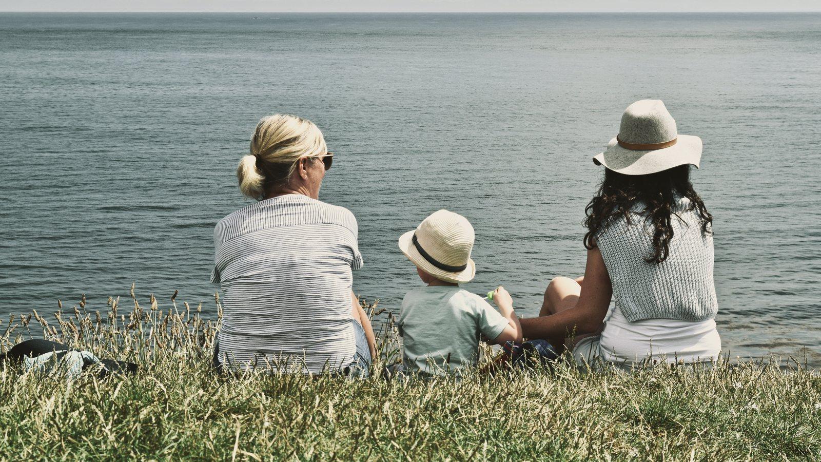 Grandmother, young child and mother sitting on a clifftop looking out to sea